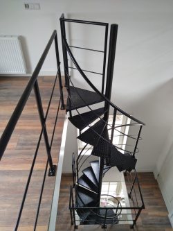 Zwarte stalen spiltrap met spijlenbalustrade voor een groot raam op een donkere houten vloer